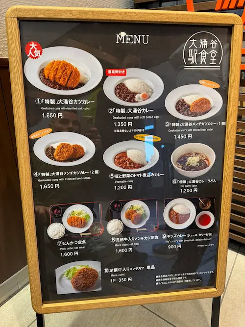 Dřevěná tabule s nabídkou jídel, fotkami karbanátů a cenami, nápisy v japonštině.